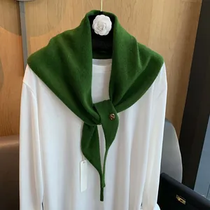 Detail eines dunkelgrünen Strickschals aus Wolle mit Metallschnalle auf weißem Shirt