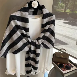 Elegant black and grey striped wool knit shawl draped over a white blouse on a hanger