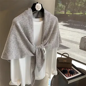 Detail of light gray knit wool shawl draped over white top in a bright natural light setting