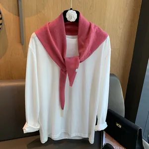 Detail eines Wollstrickschals mit runden Metallakzenten über weißem Langarmshirt