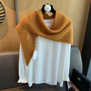 Detail eines grob gestrickten, ingwerfarbenen Dreieckstuchs über einem weißen Langarmshirt
