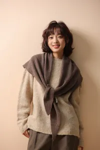 Close-up of a 100% wool knitted triangle scarf label on a model in warm light