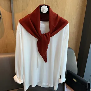 Detail eines roten Wollstrickschals über einem weißen Langarmshirt mit Kamelien-Deko