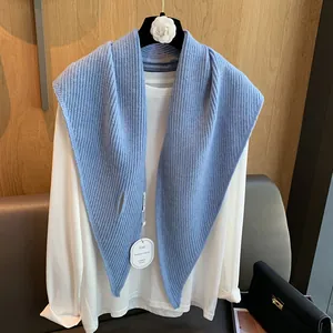 Detail eines blauen Strick-Dreiecksschals mit Schlitz-Design und Markenschild auf weißem Shirt