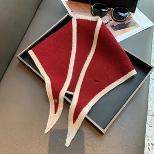 Red knit triangle scarf with cream border and metal clasp on elegant tray