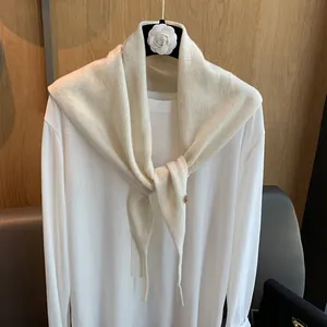 Detail eines cremeweißen Strickschals aus Wolle mit feiner Textur und Metallanhänger