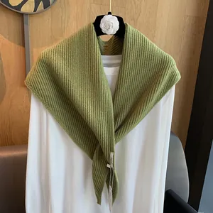 Detail eines grünen Strickschals mit Rippenstruktur und Markenetikett auf weißem Hemd