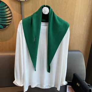 Detail view of a thick green wool triangle scarf styled on a white basic long sleeve tee