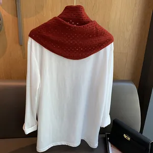 Détail d'une écharpe ajourée en laine bordeaux sur un t-shirt blanc à manches longues