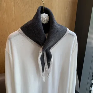 Detail of dark grey knitted triangle scarf with white contrast trim on wood background