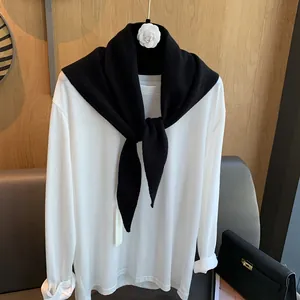 Detail eines schwarzen Strickschals aus Wolle, geknotet über einem weißen Langarmshirt