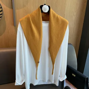 Detail eines senfgelben Strickschals, gestylt über einem einfachen weißen Langarmshirt