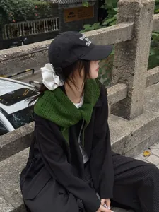 Détail d'un foulard triangle en laine vert foncé ajouré sur un trench-coat noir