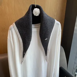 Detail of a charcoal grey knitted triangle scarf with a cream-colored border on a mannequin