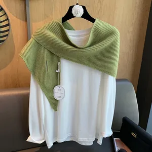 Detail eines grasgrünen Strickschals mit vertikaler Textur und Markenetiketten