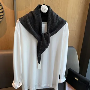 Detail eines dunkelgrauen Wollschals drapiert über ein weißes Langarmshirt