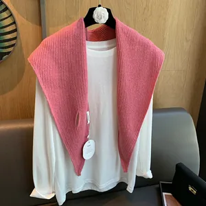 Detailaufnahme des rosa gerippten Strickschals geschichtet über einem weißen Baumwollshirt
