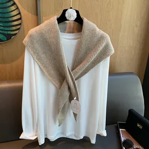 Detailansicht eines khakifarbenen Strickschals über einem weißen Langarmshirt