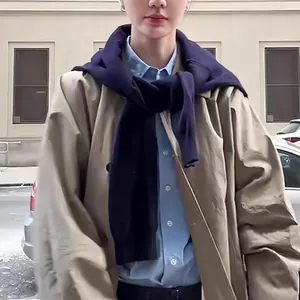 Detail of a dark blue knitted shawl draped over a khaki trench coat and blue shirt