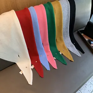Close-up of eight colored 100% wool knitted triangle scarves with metallic brand tags