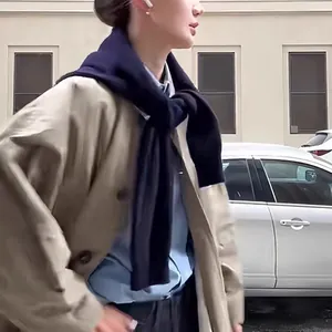 Detail of a dark blue knitted shawl styled over a khaki trench coat for layering