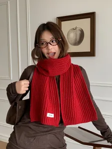 Close-up of a chunky red knit scarf with a minimalist white fabric label and soft texture