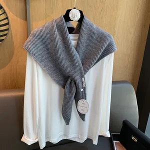 Detail eines grauen Grobstrick-Dreieckstuchs mit weicher Textur und Designer-Etikett