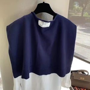 Detailed view of dark blue knit shawl vest paired with a white shirt and brand neck label