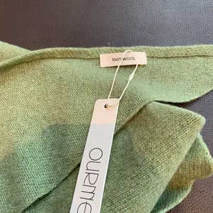 Detailaufnahme des grünen Strickschals aus 100% Wolle mit feiner Textur und Etikett