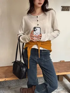 Détail d'une écharpe en laine jaune ajourée nouée à la taille sur un cardigan blanc