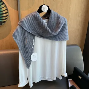 Detail eines grau gestreiften Strickschals kombiniert mit einem weißen Langarmshirt