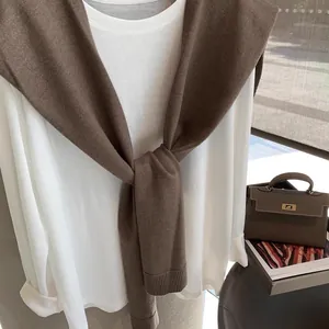 Close-up of brown knitted shawl layered over white long-sleeve tee for trendy spring styling