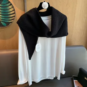 Detail eines schwarzen Strickschals, getragen über einem weißen Langarm-T-Shirt