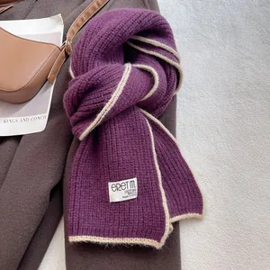 Détail d'une écharpe en tricot violet avec bordure beige et écusson de logo minimaliste