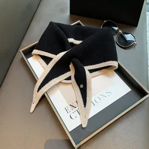 Close-up of contrast knit scarf with metal button on dark tray with accessories