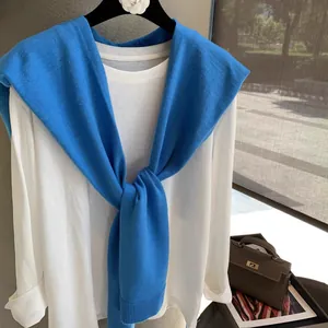 Detail of blue knitted shawl over white long sleeve top showing refined ribbed edge texture