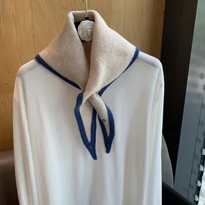 Detail of beige knit neck warmer with dark blue ribbed trim on a white long sleeve shirt