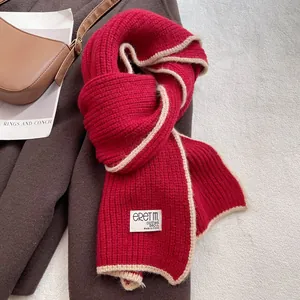 Gros plan sur l'écharpe en maille rouge avec bordure beige et étiquette tissée