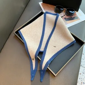 Close-up of cream knit triangular scarf with navy trim and metal button on a tray