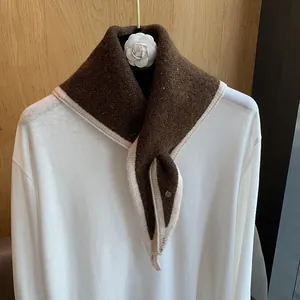 Detail of dark brown knitted scarf with cream trim and metallic tag on a white shirt