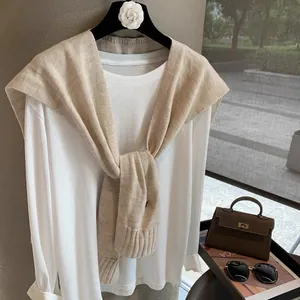 Detailed knit texture of a beige wool shawl with ribbed edges on a white long sleeve top