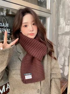 Close-up of brown chunky knit wool scarf featuring a white textile label on grey coat