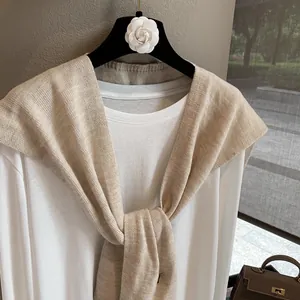 Detailed texture of beige wool knit shawl layered over a white long-sleeve T-shirt