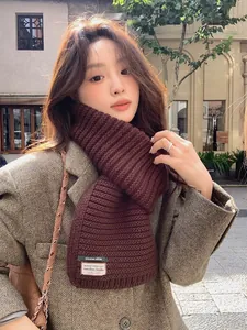 Detailed close-up of dark brown knit scarf with vintage decorative labels and chunky texture