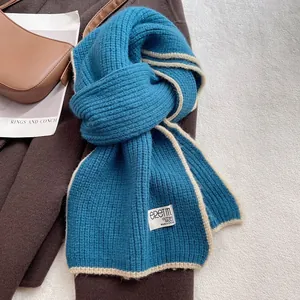 Gros plan d'une écharpe en laine bleu paon avec bordure beige et étiquette tissée