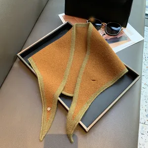 Detail of a brown knit triangle scarf with green edges and a silver metal buckle