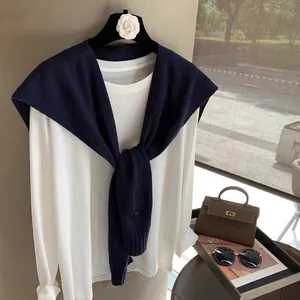 Close-up of a navy wool knit shawl knotted over a white long-sleeved tee for a layered look