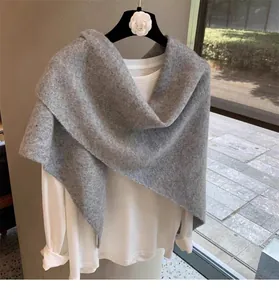 Close-up of light grey wool blend knitted shawl with thick texture on white top