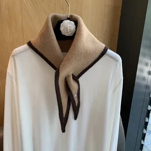 Detailed knit texture of a camel triangle scarf with contrast piping and metal button