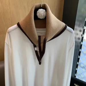 Detail of a minimalist knit neck warmer with metal buttons on a white shirt top